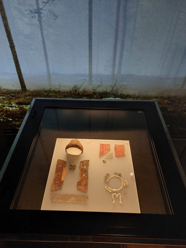 På bilden syns en monter med föremål från barngravar, balnad annat visas delar av en gravdräkt och en begravningskrans.