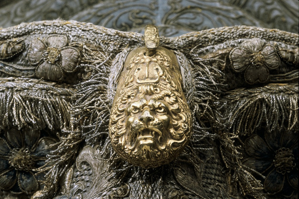 Ett lejonhuvud med man av förgylld metall sitter på en sadel och utgör sadelknapp.