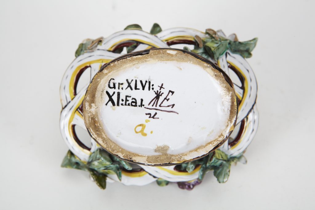 Undersidan av fajansskål med skrivna signaturer och museimärkning.