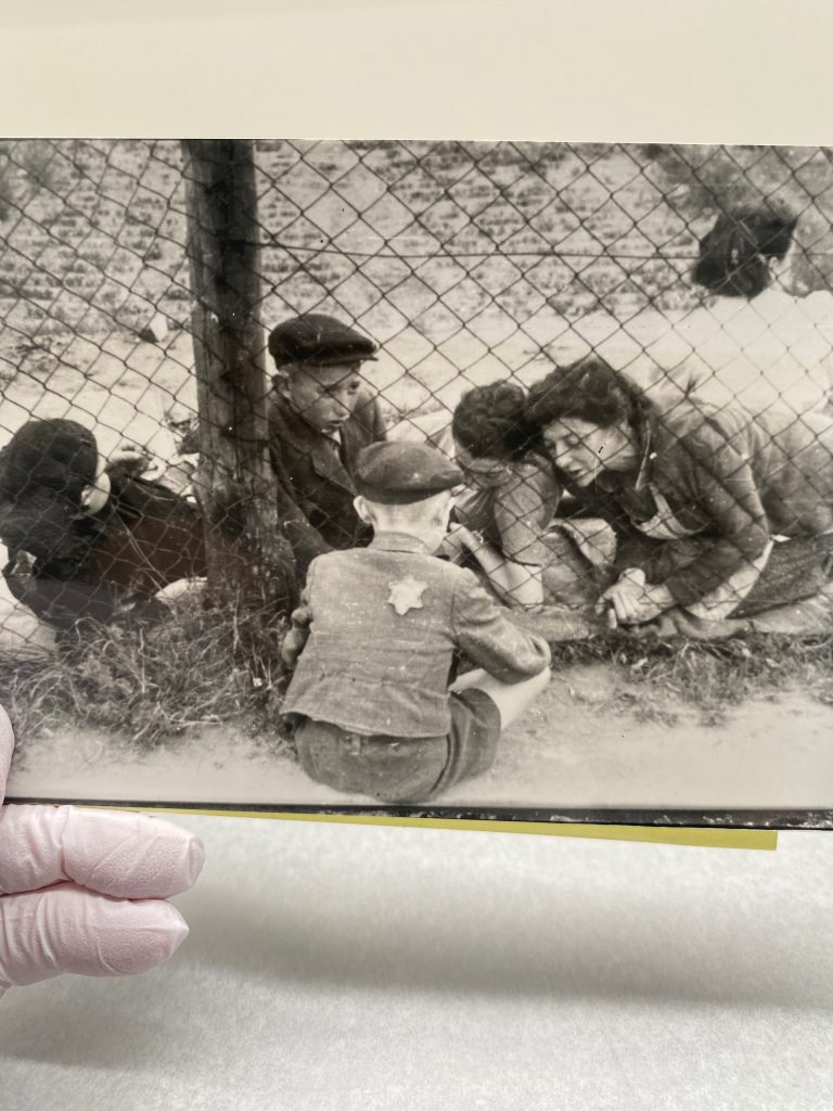 Foto av ett stängsel. På ena sidan sitter ett barn. På andra sidan en kvinna och tre barn.