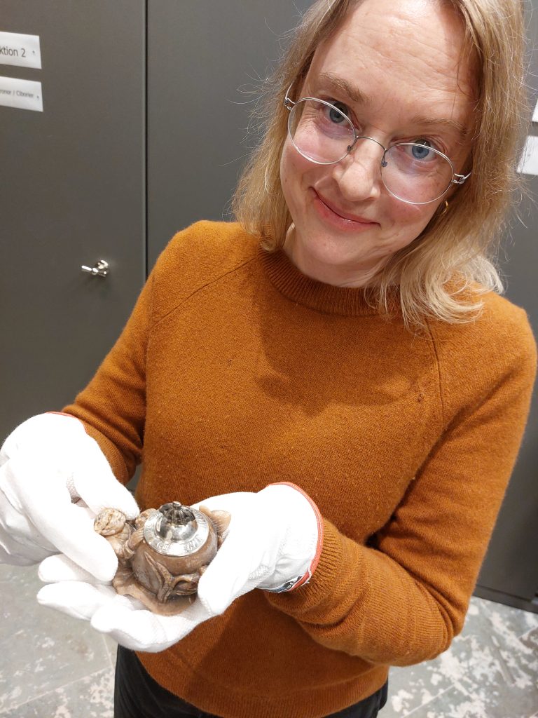 Antikvarie Jenny Nyberg syns i halvkroppsbild, tittandes leendes in i kameran med bläckhornet i handen.