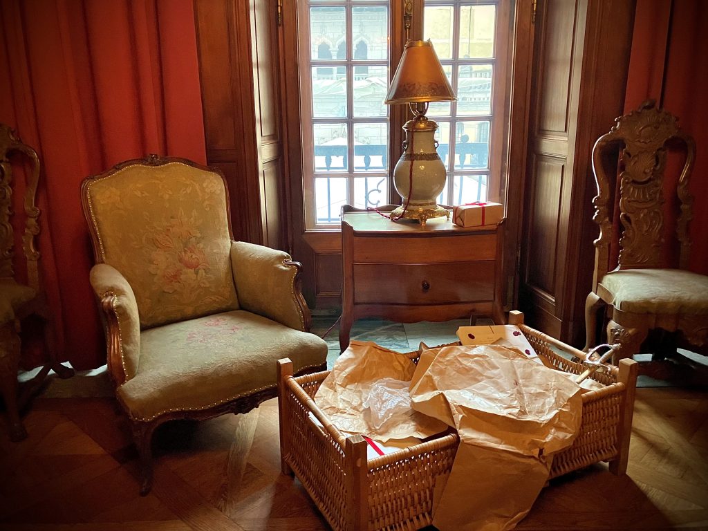 Fotografi från ett ombonat rum. En korg med paket står framför en fåtölj.