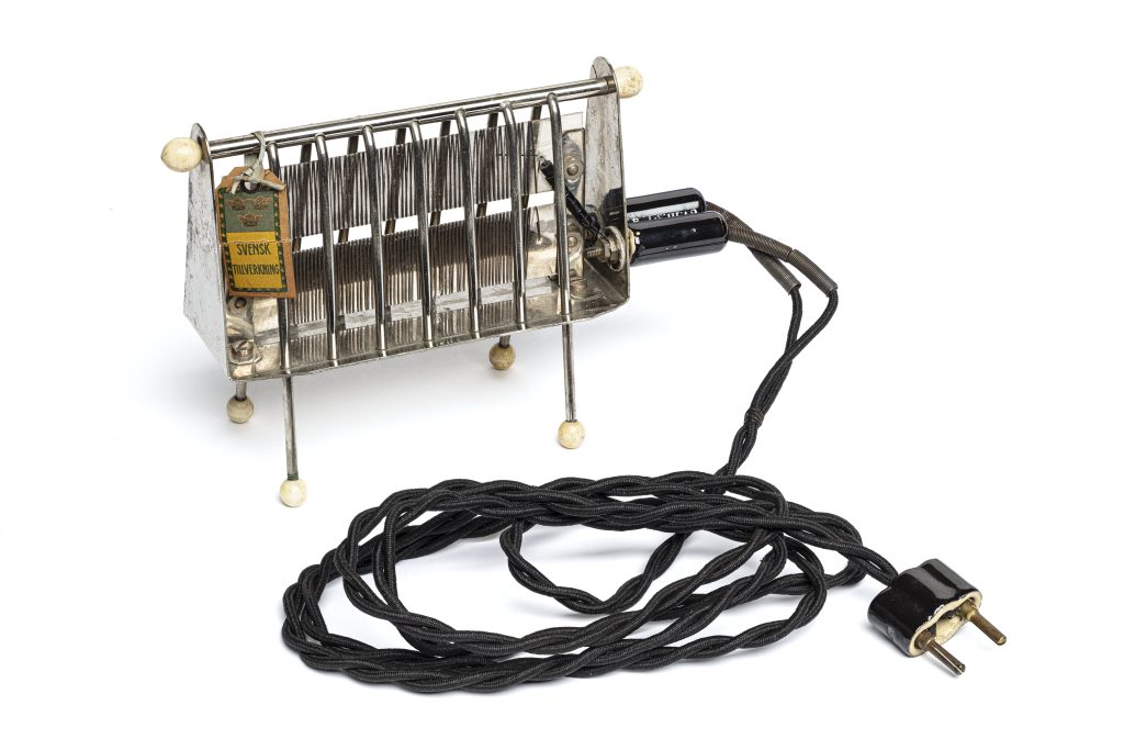 Gammaldags elektrisk brödrost av blank metall med svart sladd.