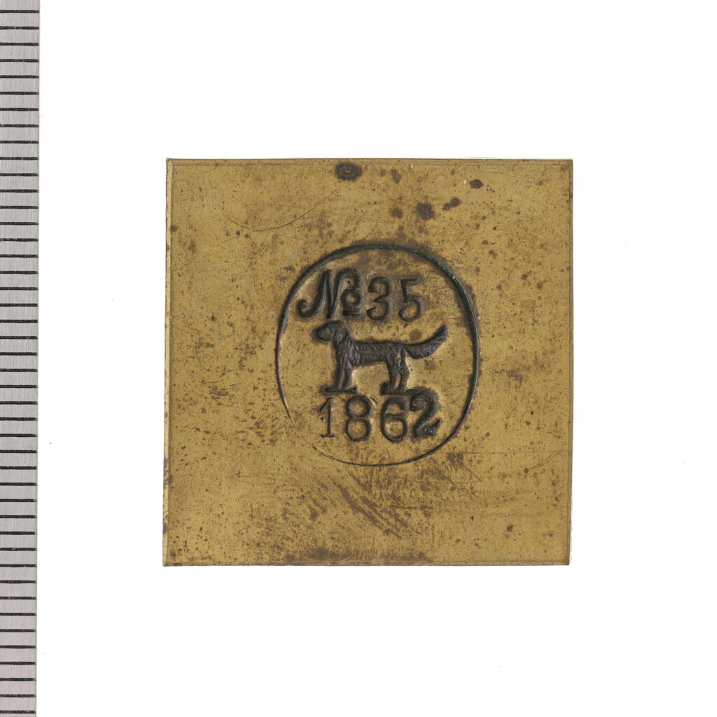 Fyrkantigt metallmärke med hund och siffror.