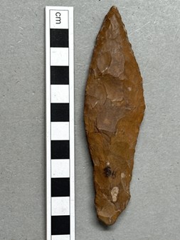 Spetsig bit av flinta som ligger bredvid en linjal.