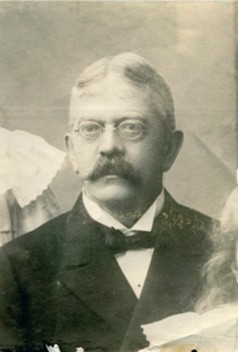 Svartvitt foto av man med glasögon och stor mustasch.