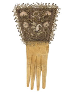 Gulvit handske med krage av spets som är dekorerad med en pelikan och blommor.